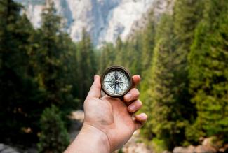 person holding compass facing towards green pine trees by Jamie Street courtesy of Unsplash.